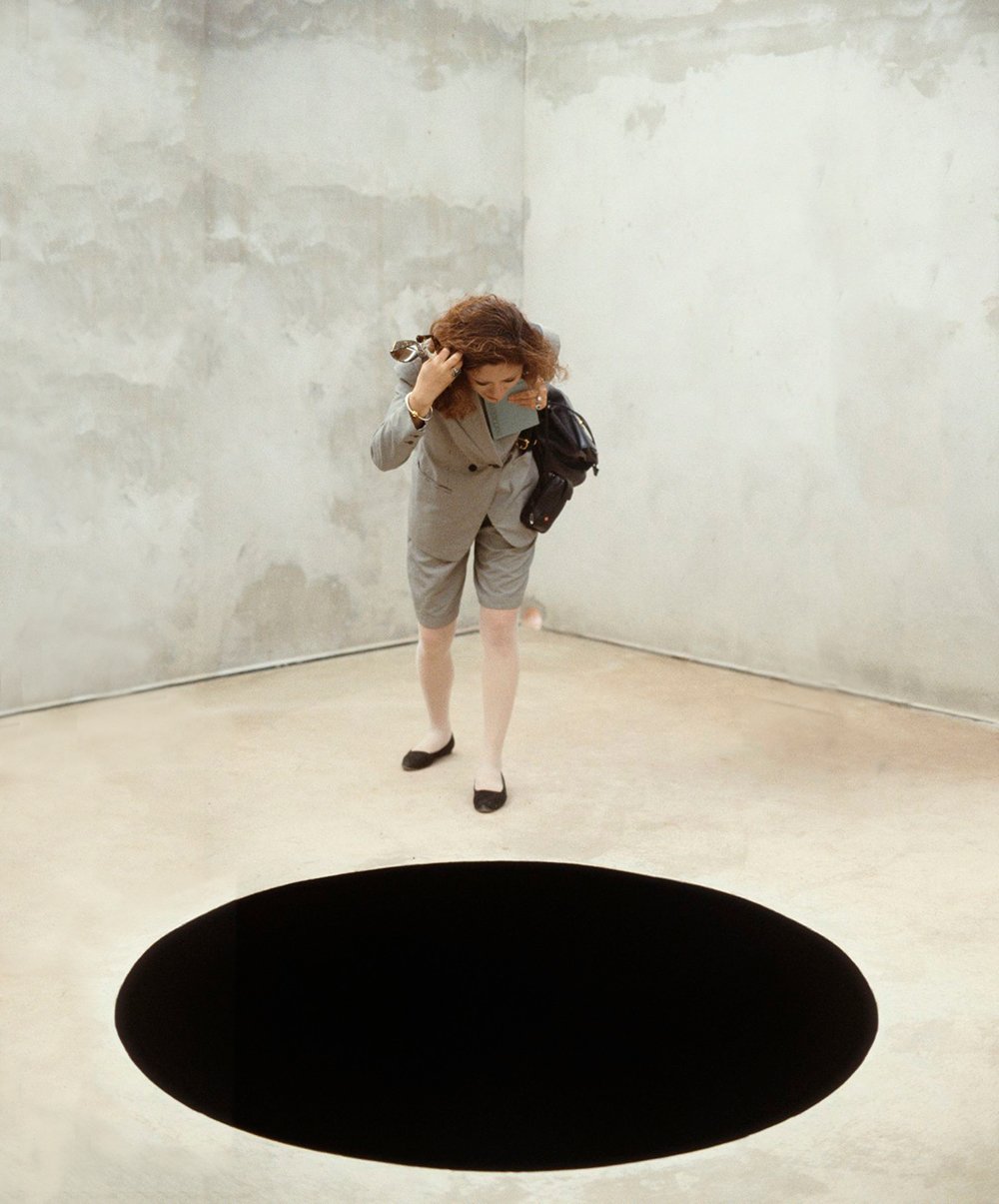 a woman stares into a black hole on the ground